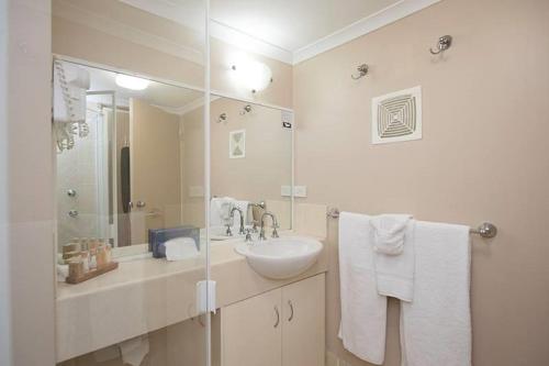 Baño blanco con lavabo y espejo en Harbour Sails Motor Inn en Gladstone