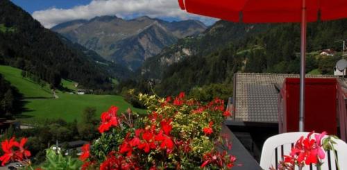 a balcony with red flowers and an umbrella and mountains at Residence Pichler Apartment 1 in San Leonardo in Passiria