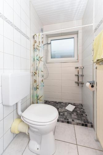 a white bathroom with a toilet and a window at Hotel-Pension Janssen - Gästehaus Huus an't Deep in Neuharlingersiel