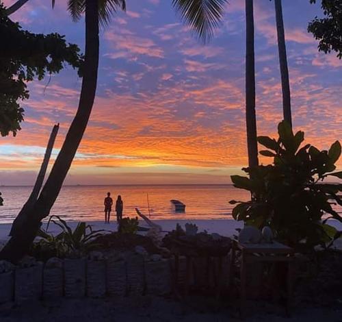 two people standing on the beach at sunset at Tria Maria Cottage in Ngurblut