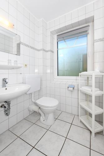 a white bathroom with a toilet and a sink at Hotel-Pension Janssen - Gästehaus Huus an't Deep in Neuharlingersiel