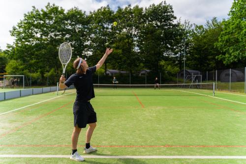 a woman serving a tennis ball on a tennis court at SportsPark Blaavandshuk Resort in Oksbøl