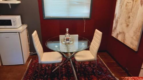 a glass table with white chairs and a bottle on it at Furrows Lodge in Nieu-Bethesda