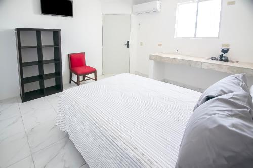 a white bedroom with a bed and a red chair at OYO Hotel Plaza Las Torres, Cabo San Lucas in Cabo San Lucas