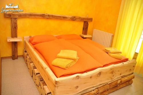 een houten bed met oranje lakens en handdoeken erop bij Baita Carosello Apt 4 by Livigno Accomodation in Livigno