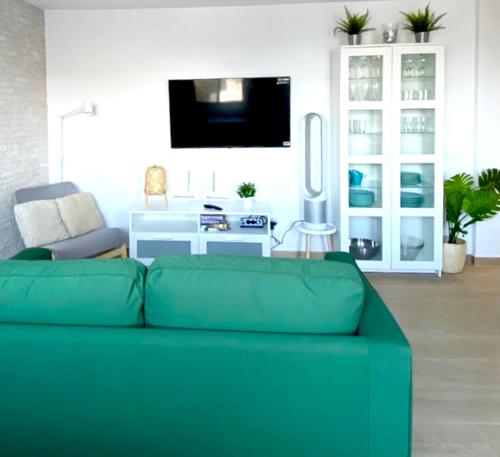 a living room with a green couch and a tv at SUNRISE ESQUINZO, paraíso de sol & playa & paz in Playa Jandia