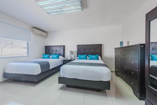 two beds in a bedroom with blue pillows at Ayenda Suites Ejecutivas Monterrey in Monterrey