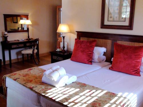 a bedroom with a bed with red pillows and a desk at De Hoek Manor in Stellenbosch