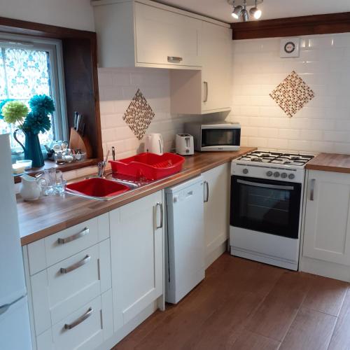 a kitchen with white cabinets and a sink and a stove at Honeysuckle Cottage in Wiggenhall Saint Germans