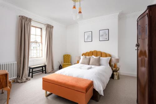 um quarto com uma cama branca e um repousa-pés laranja em Luxe Design - Grade II Listed Cottage - Heart of Alnwick em Alnwick