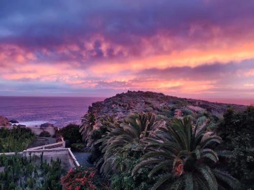 a sunset over a hill with palm trees and the ocean at Finca La Punta in Icod de los Vinos