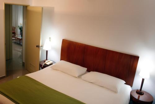 a bedroom with a white bed with a wooden headboard at HOTEL ALTAMIRA SUITES in Caracas