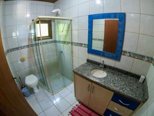uma casa de banho com um chuveiro, um lavatório e um espelho. em Casa Vista Privilegiada: Piscina e Conforto em Garopaba