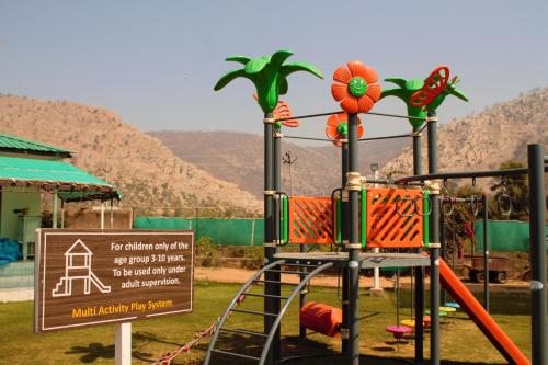 a playground with a slide and a sign with mountains in the background at Shivir Aranya - Wilderness Resort in Alwar