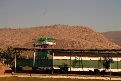 a building with a grass roof with a hill in the background at Shivir Aranya - Wilderness Resort in Alwar