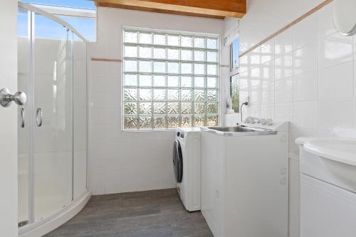 een witte badkamer met een wastafel en een wasmachine bij Taranui Escape - Mangawhai Heads Holiday Home in Mangawhai