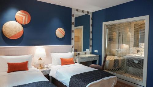 2 Betten in einem Zimmer mit blauen Wänden und orangefarbenen Kissen in der Unterkunft Sojourn Guest House Melaka in Malakka