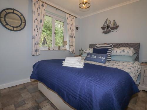 a bedroom with a bed with a blue comforter and a window at Merryfield Lodge in Liskeard