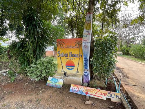a sign sitting next to a tree on a dirt road at Sabai Beach Resort in Ko Mak