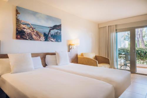 two beds in a hotel room with a view of the ocean at Iberostar Waves Pinos Park in Font de Sa Cala