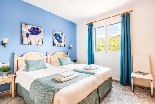 Dos camas en una habitación con paredes azules y una ventana. en Villa Karoline, en Cala en Forcat