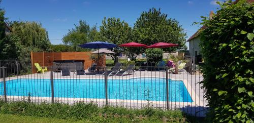 uma piscina com guarda-sóis, mesas e cadeiras em Gîte et chambres d'hôtes Le Chêne Billault em Pouant