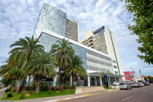 a tall building with palm trees in front of a street at Slaviero Rondonópolis Centro in Rondonópolis