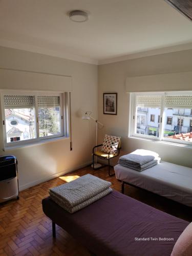 Cette chambre comprend deux lits, une chaise et deux fenêtres. dans l'établissement Alex Point - Guest House, à Viana do Castelo