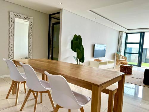 une salle à manger avec une table en bois et des chaises blanches dans l'établissement Seacrest Luxury Beachfront Apartment - Blouberg Beach, à Bloubergstrand
