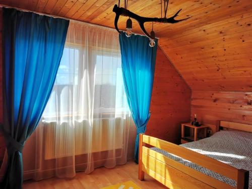 a bedroom with a bed and a window with blue curtains at Jugul Țăranului Agropensiune Polovragi, Gorj in Polovragi