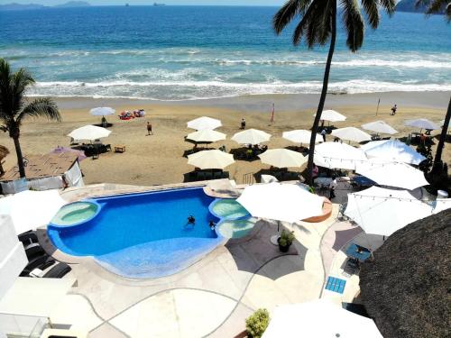 a swimming pool next to a beach with umbrellas at Mar Celeste in Manzanillo