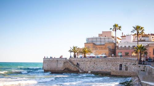 a brick wall next to the ocean with palm trees at Bo&Co Apartments in Sitges