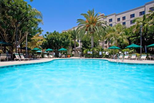 Sonesta ES Suites Anaheim Resort Area في أنهايم: مسبح كبير مع كراسي ومظلات في الفندق
