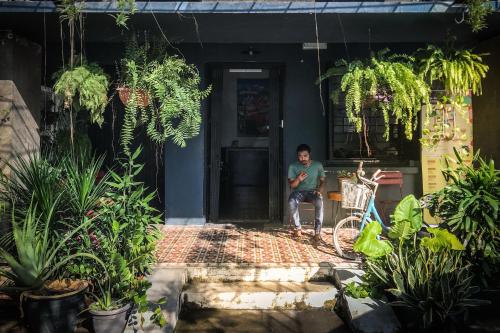 a man sitting in the doorway of a house with plants at The Brownstone Hostel & Space in Ipoh