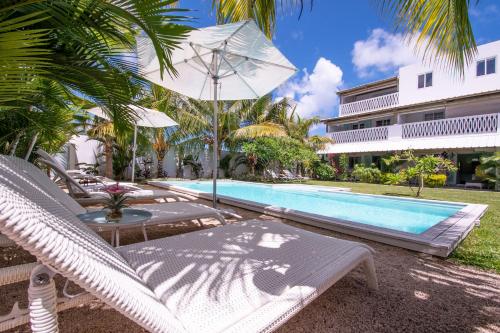 a pool with lounge chairs and an umbrella next to a resort at Le Mandala Moris in Pointe aux Canonniers