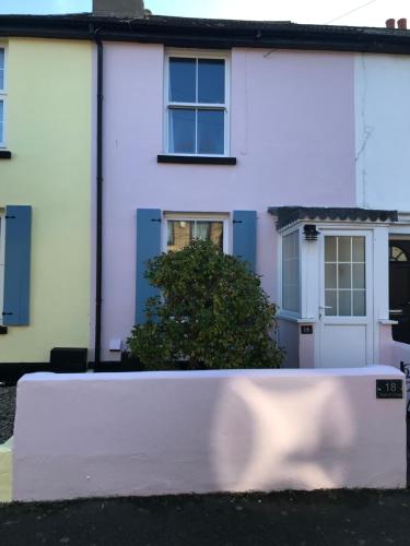 a white house with blue windows and a bush at Seashell Cottage in Deal