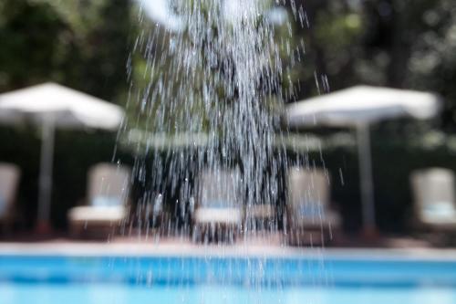 a water fountain in a pool with chairs and umbrellas at Hotel 1908 in Forte dei Marmi