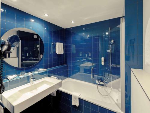 ein blau gefliestes Bad mit einer Badewanne und einem Waschbecken in der Unterkunft Congress Hotel Mercure Nürnberg an der Messe in Nürnberg