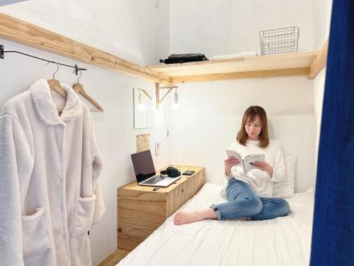 una chica sentada en una cama leyendo un libro en Blue Hour Kanazawa, en Kanazawa