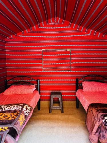 Una habitación roja con dos camas y un taburete dentro. en Wadi Rum Pyramids Camp, en Wadi Rum