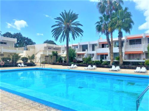 a large swimming pool with palm trees and buildings at Cozy one bedroom apartment with spacious terrace. Pool and garden view in Costa Del Silencio