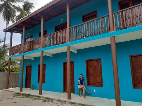 una mujer se sienta frente a un edificio azul en Vila Samin Moitas en Praia de Moitas