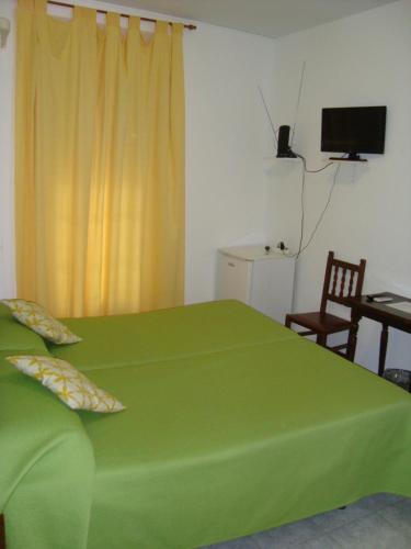 a bedroom with a green bed with a table and a television at Hostal Durán in Alora
