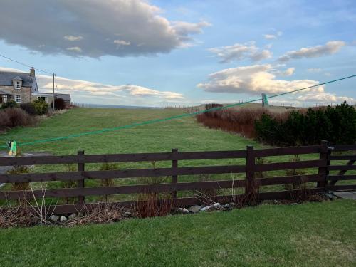 a fence in front of a field with a house at Traditional 2 bed croft in Portskerra