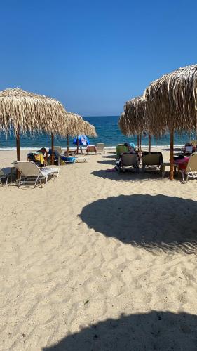 a beach with chairs and straw umbrellas and the ocean at T H E BERLIN Studios and Suites in Nea Vrasna