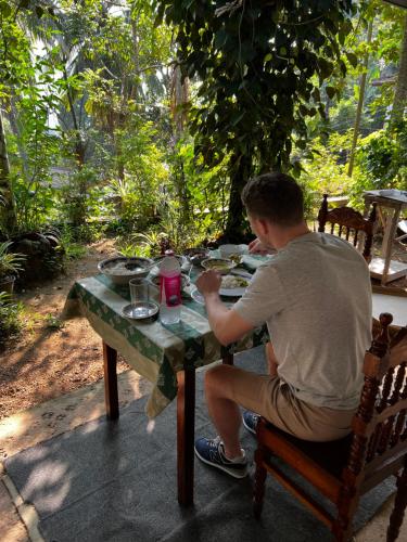 un hombre sentado en una mesa con un plato de comida en Summer Ridge - Homestay, en Ratnapura