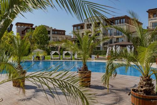 a swimming pool with palm trees in front of buildings at Green Life Beach Resort Apartment in Sozopol