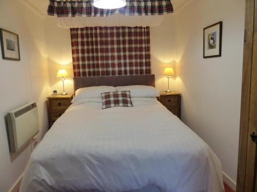 a bedroom with a large white bed with two lamps at Crepigill Cottage in Portree