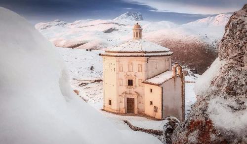 a building in the snow with a mountain in the background at IL BORGO DI ROCCA CALASCIO in Calascio