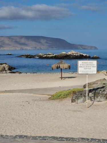 a sign on a beach with an umbrella at Cabañas Aquila D'Arroscia in Bahia Inglesa